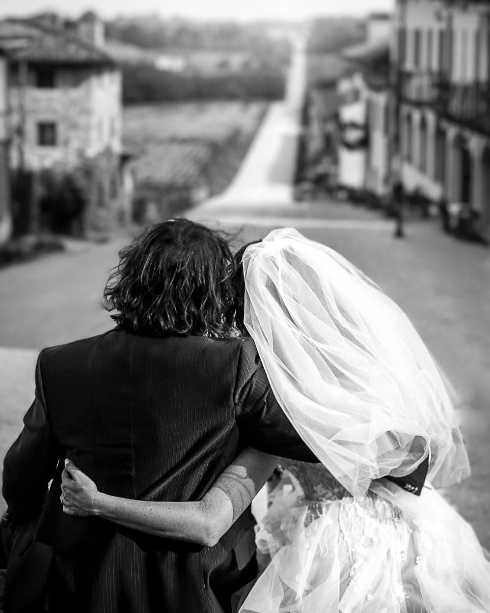 Sposi di spalle abbracciati su una strada di campagna in bianco e nero, con il velo mosso dal vento, matrimonio a Udine