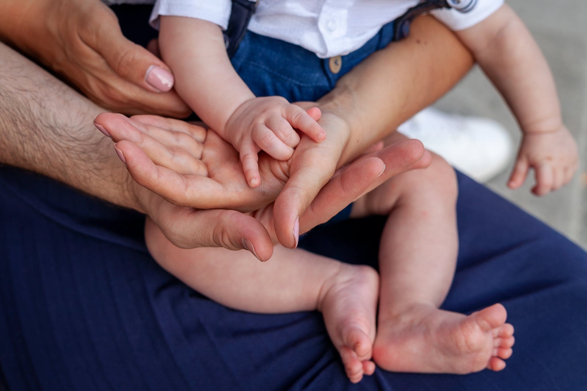 Mani di un adulto che stringono i piedini e le manine di un bambino piccolo seduto sulle gambe, primo piano
