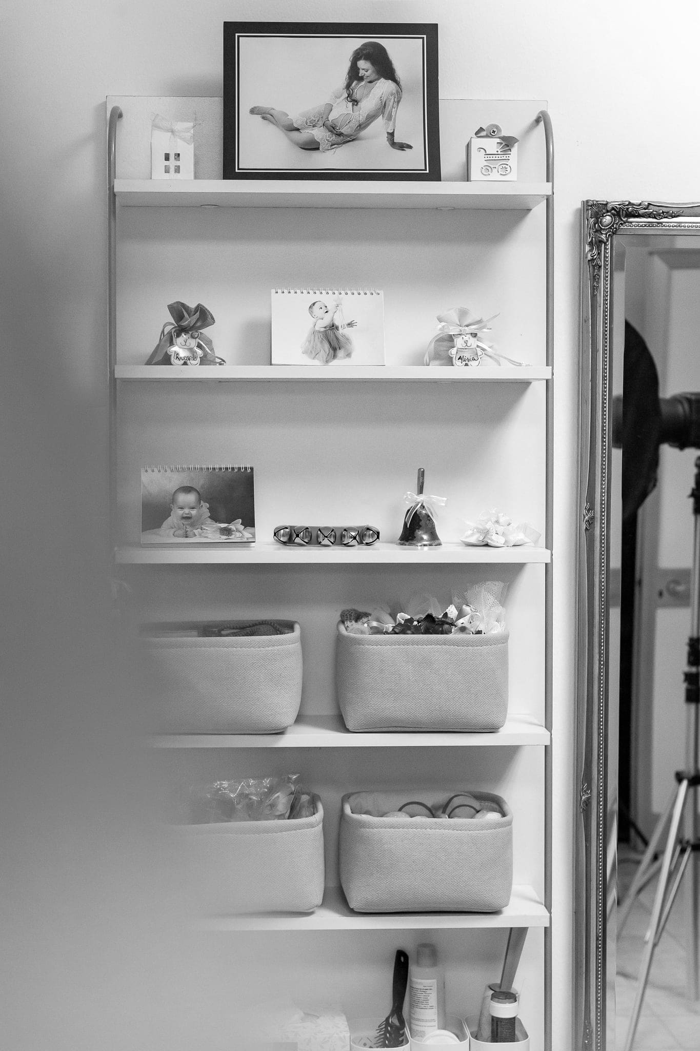 Mensola nello studio con foto incorniciata di una gestante, calendario e cestini con accessori, accanto a uno specchio