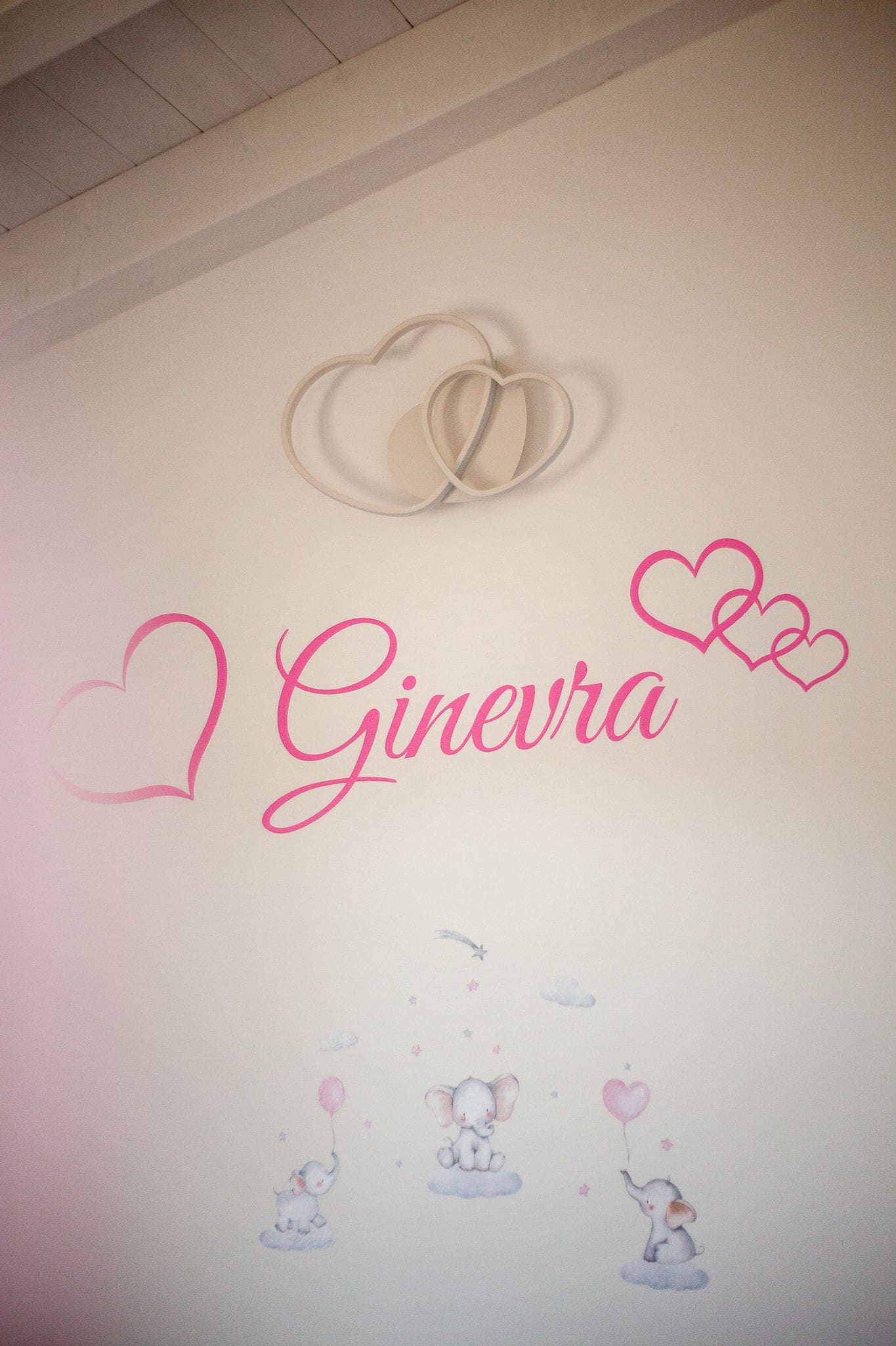 Scritta rosa con cuori e piccoli elefanti disegnati sulla parete della cameretta, che dà il benvenuto alla piccola