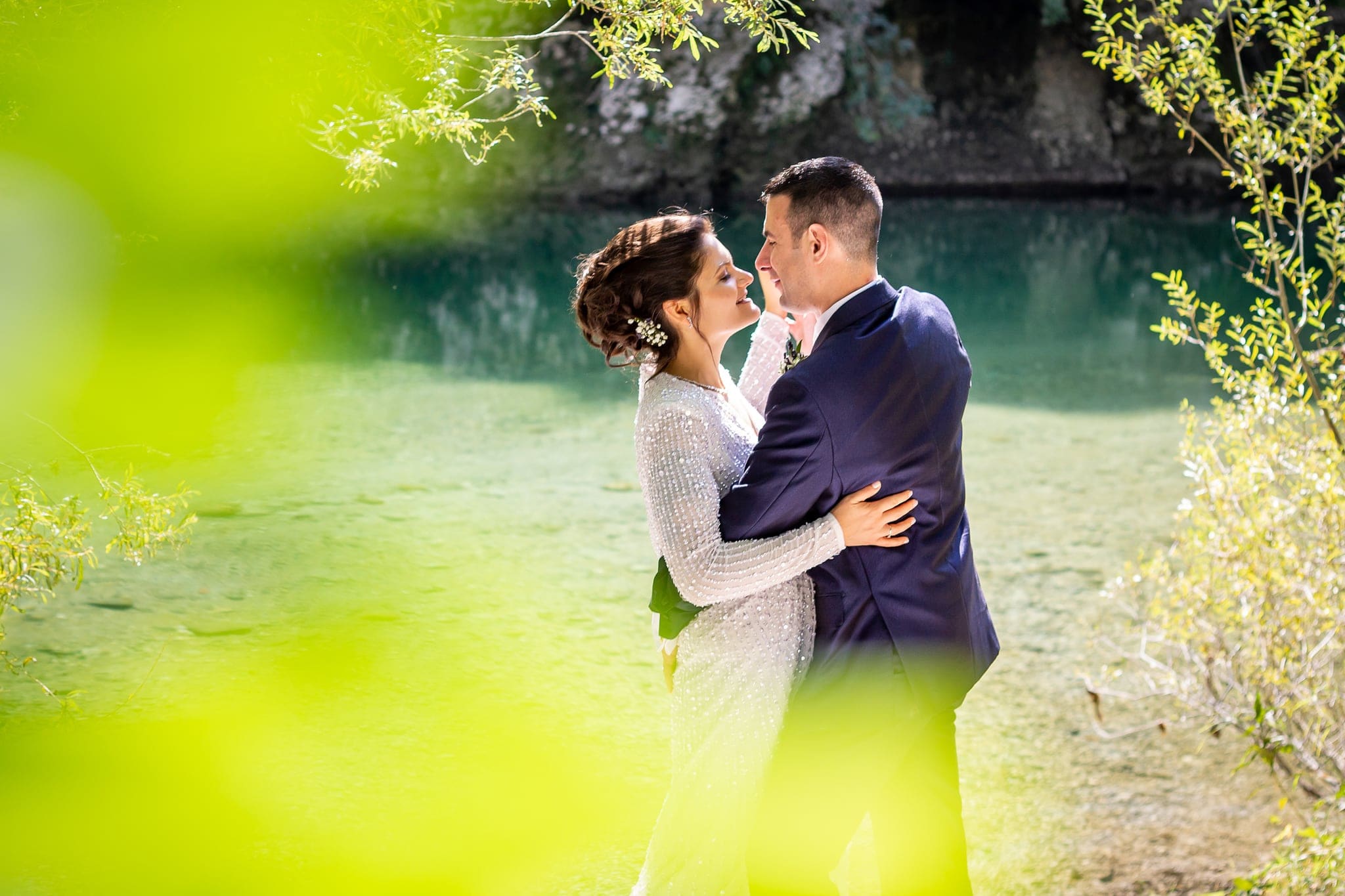 Sposa e sposo si abbracciano sulla riva di un laghetto tra riflessi verdi, matrimonio a Cividale del Friuli