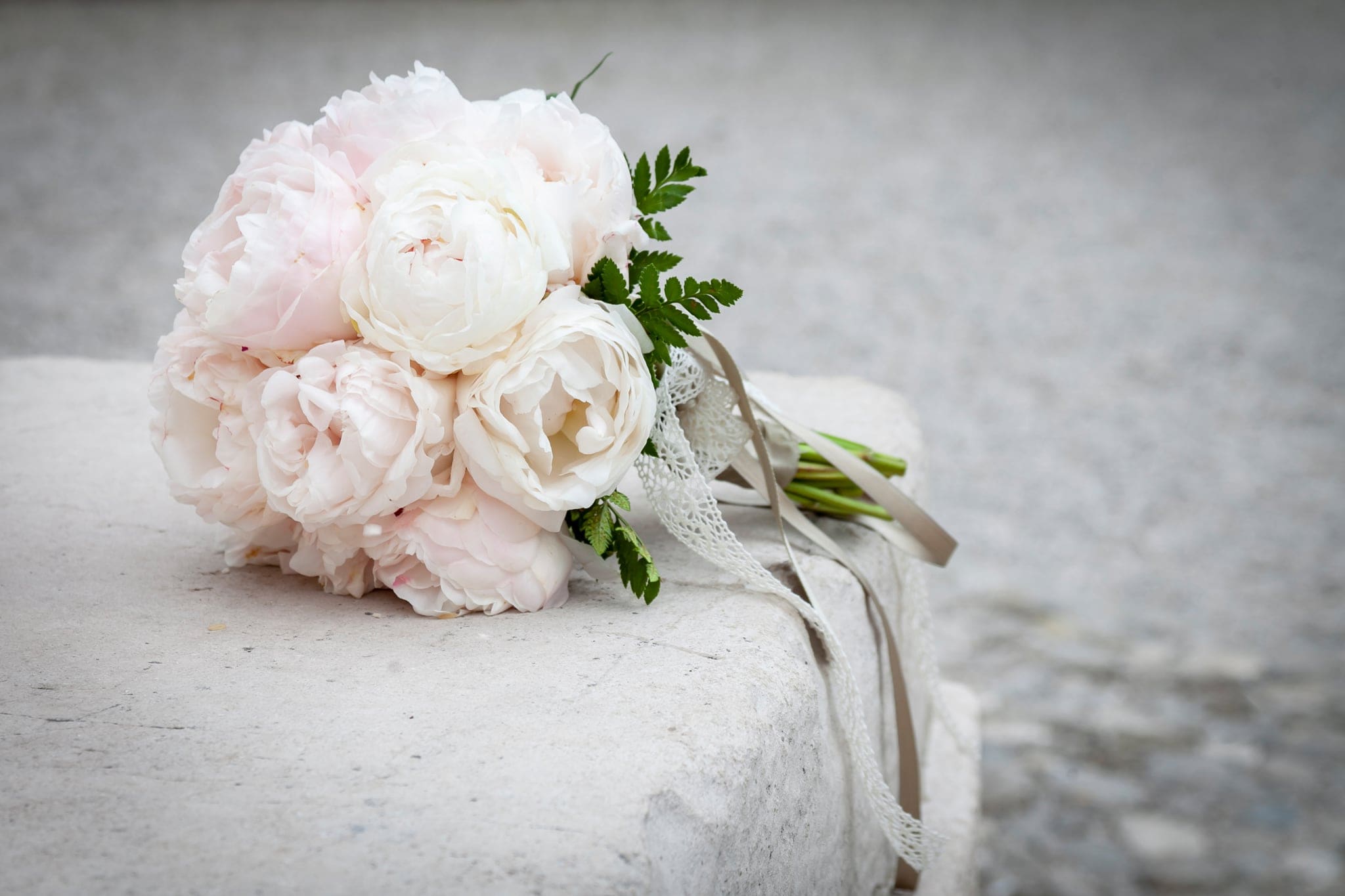 Bouquet di peonie rosa e bianche con nastri e pizzo, appoggiato su un muretto in pietra, matrimonio a Udine