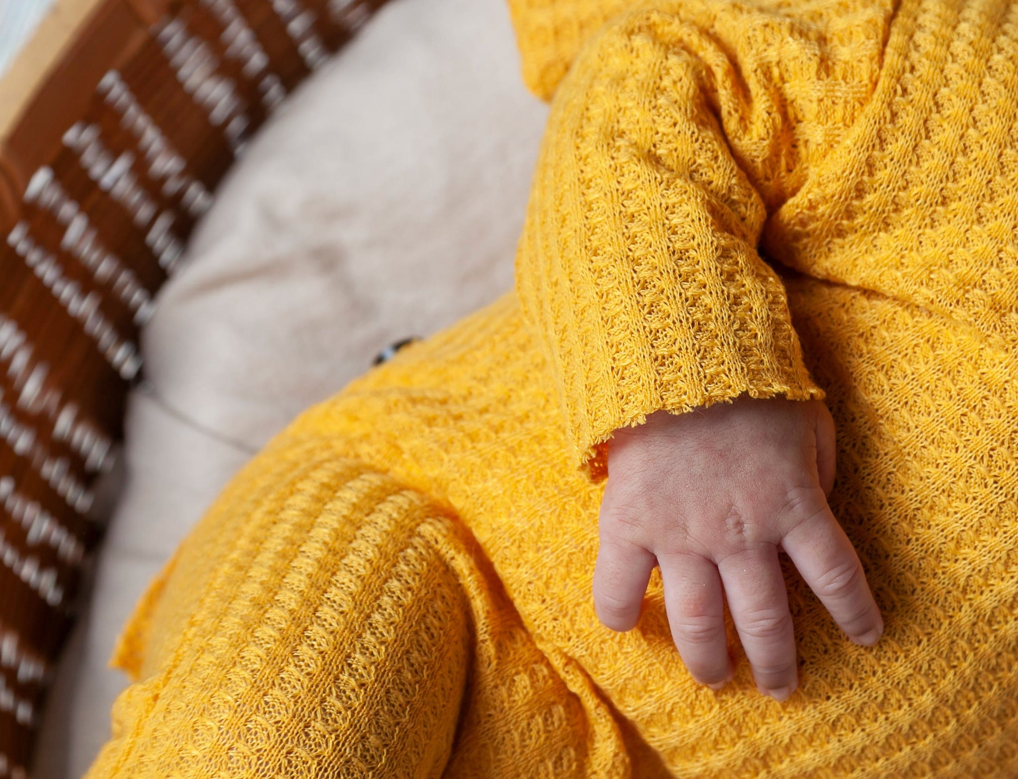 Dettaglio della manina di un neonato appoggiata sulla tutina gialla a trama a nido d'ape, dentro un cesto di vimini.