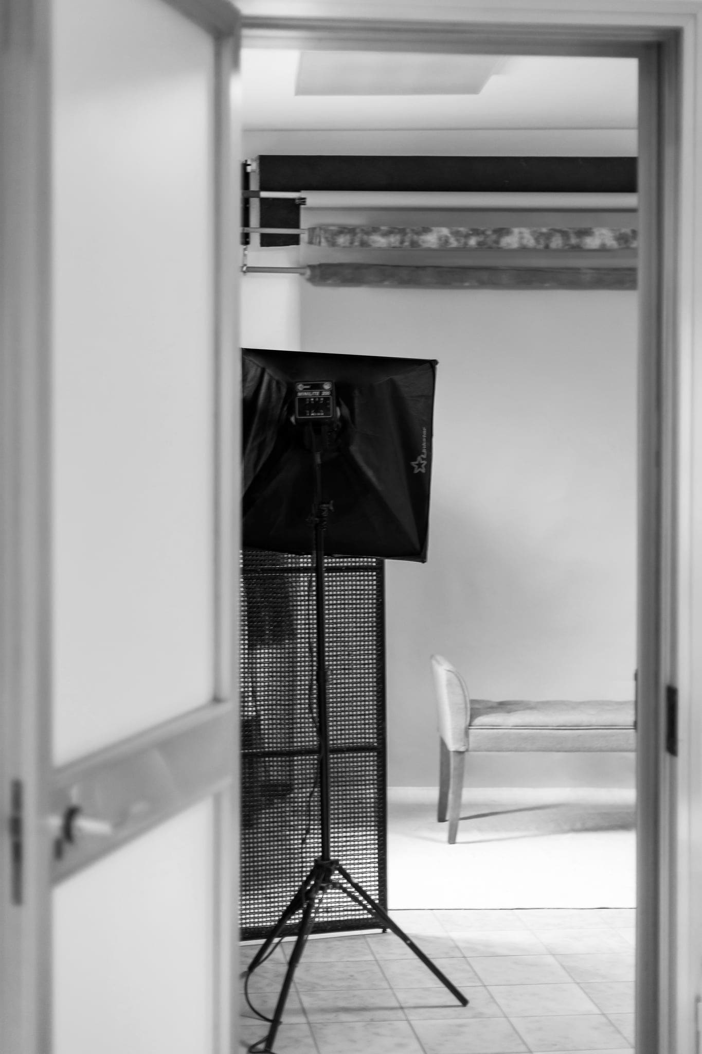 Porta aperta sullo studio fotografico, con softbox su treppiede e panca sullo sfondo, in bianco e nero