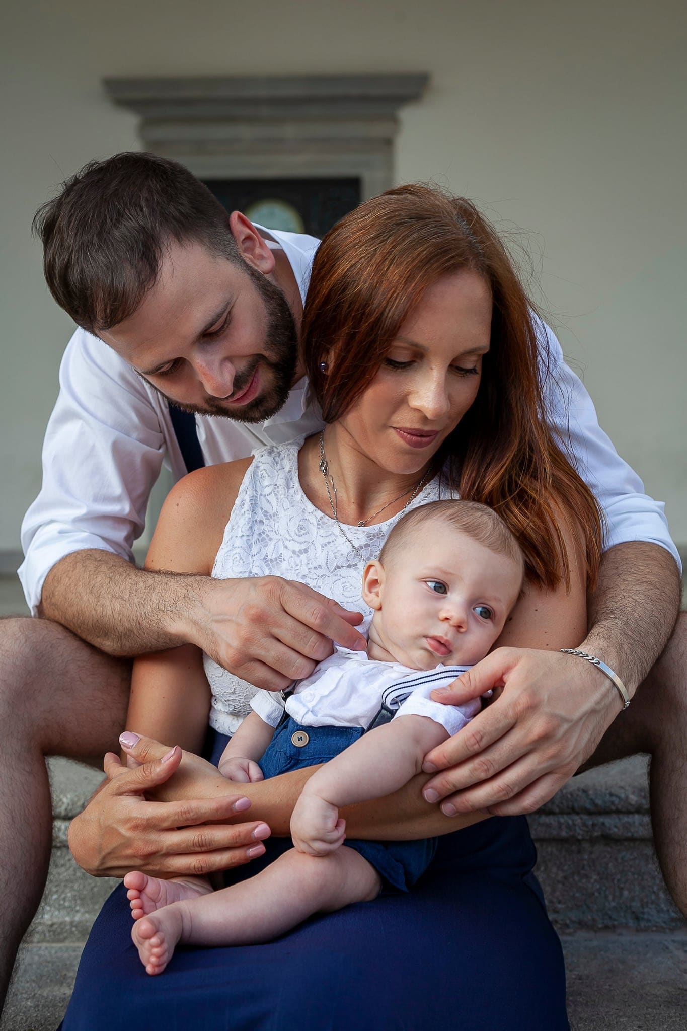 Papà e mamma seduti su dei gradini all'aperto stringono tra le braccia il bimbo, che guarda lontano