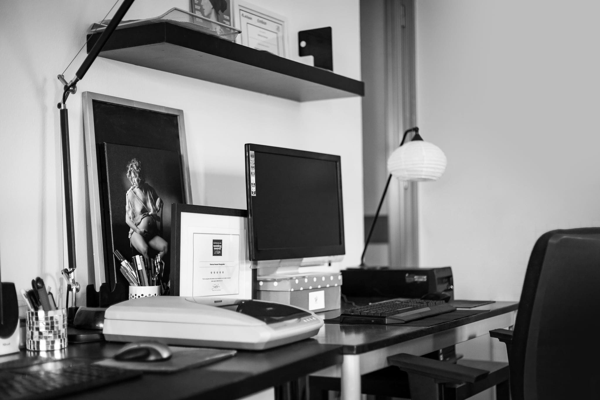 Scrivania dello studio con computer, lampada, portapenne e quadro in bianco e nero appeso al muro