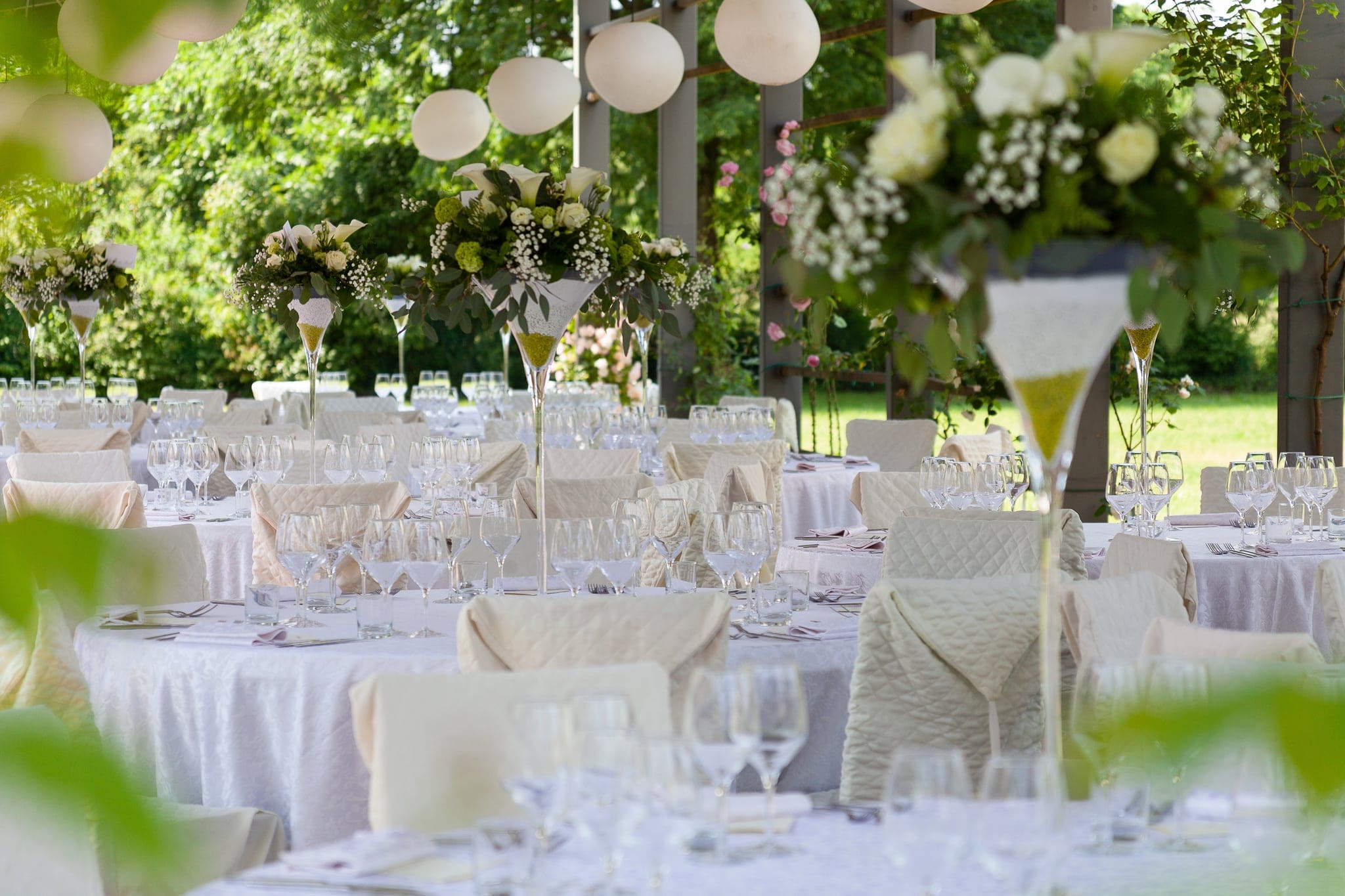 Tavoli apparecchiati in giardino con centrotavola di fiori bianchi e lanterne di carta, matrimonio a Villa Nachini