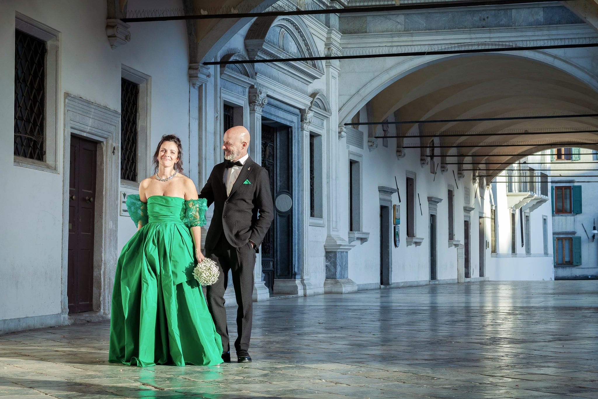 Sposa in abito verde smeraldo e sposo in smoking sotto un portico antico, con il bouquet di gypsophila, matrimonio a Udine
