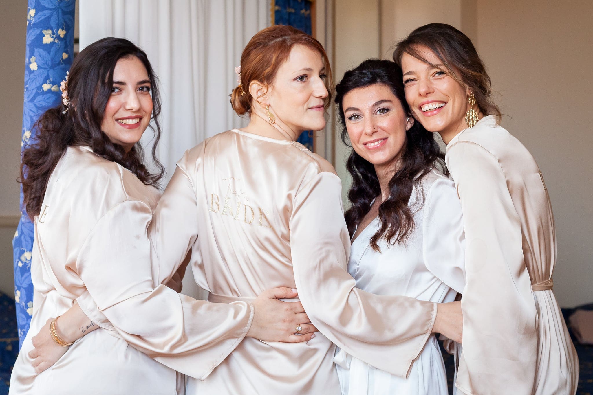 Sposa abbracciata alle amiche in vestaglie di raso color champagne, tutte sorridenti, durante la vestizione a Trieste
