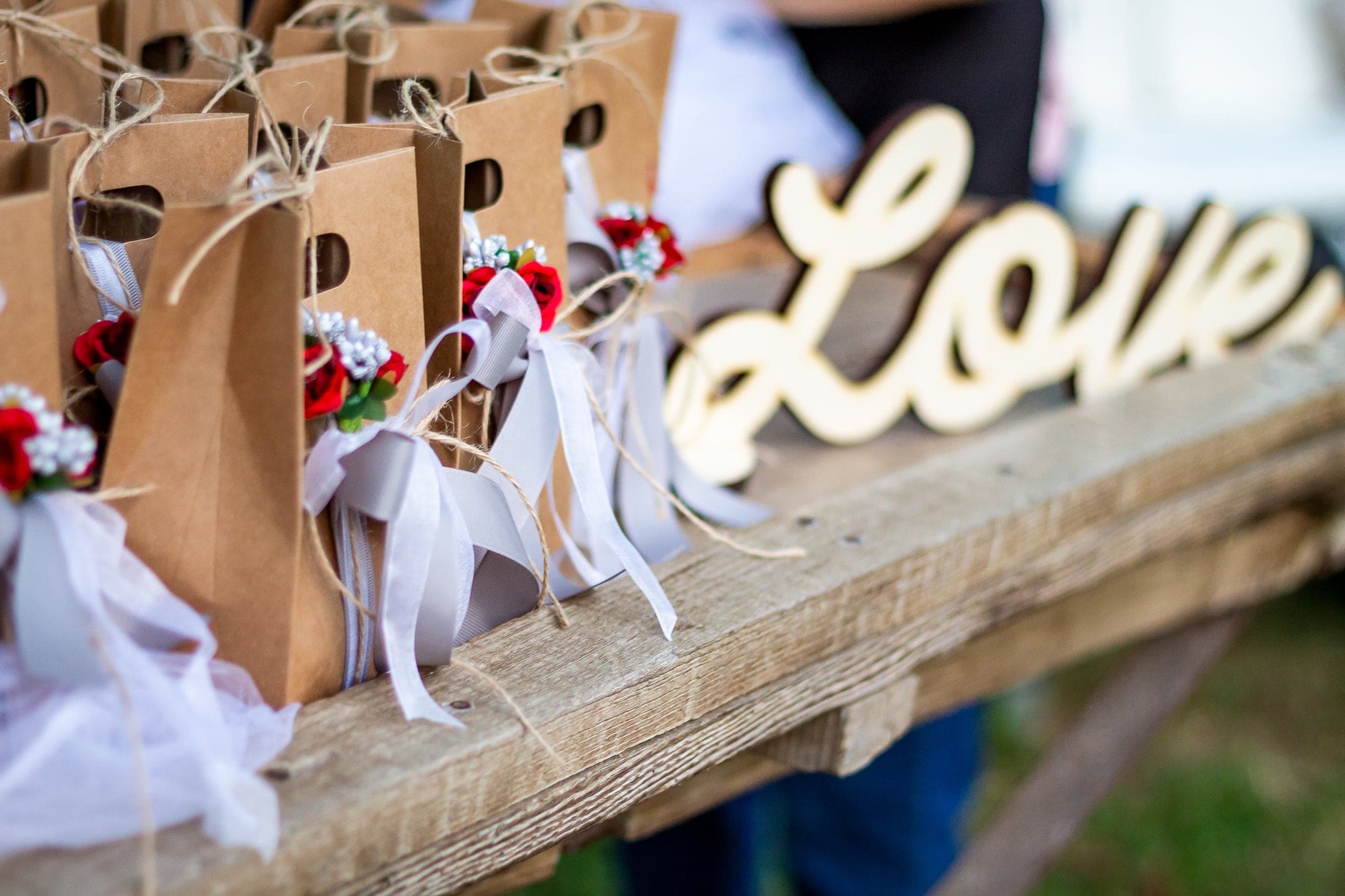 Bomboniere in sacchetti di carta kraft con fiori rossi e nastri, accanto alla scritta Love su una trave di legno, a Udine