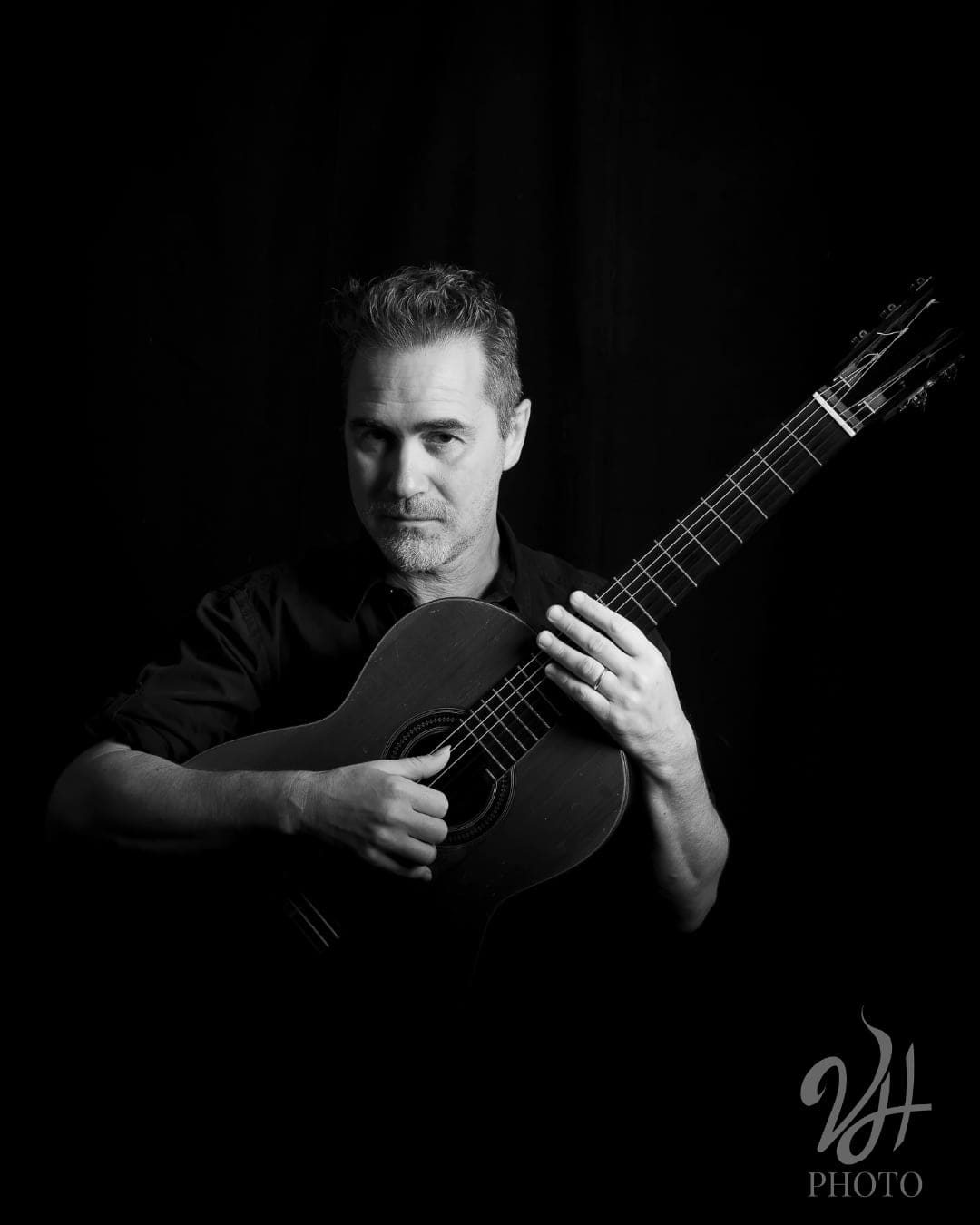 In bianco e nero, uomo con la chitarra classica in mano, sguardo intenso, illuminato su fondo nero in un ritratto di studio