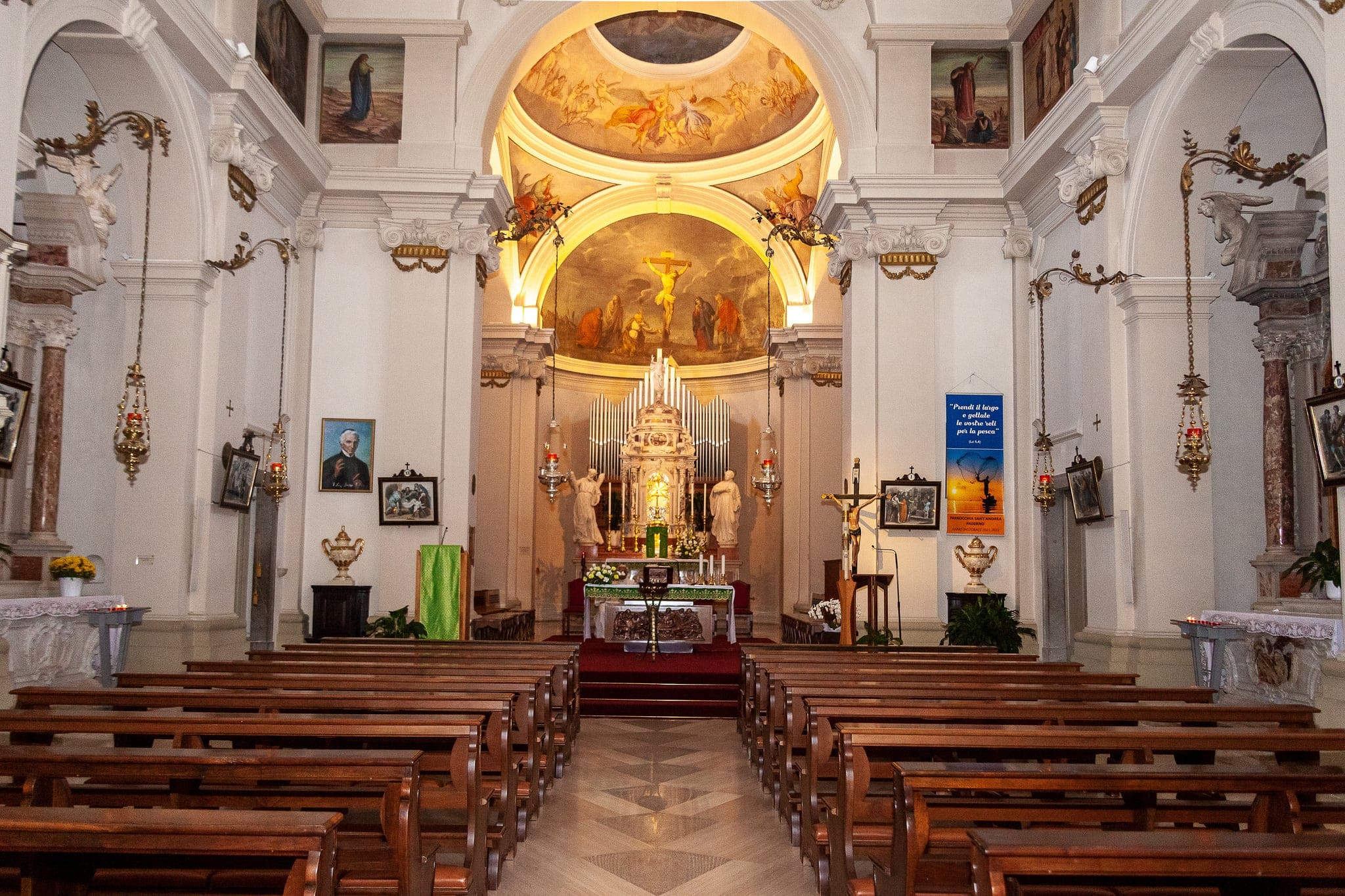 Interno di una chiesa barocca con panche di legno, navata centrale e altare illuminato con affreschi sulla volta