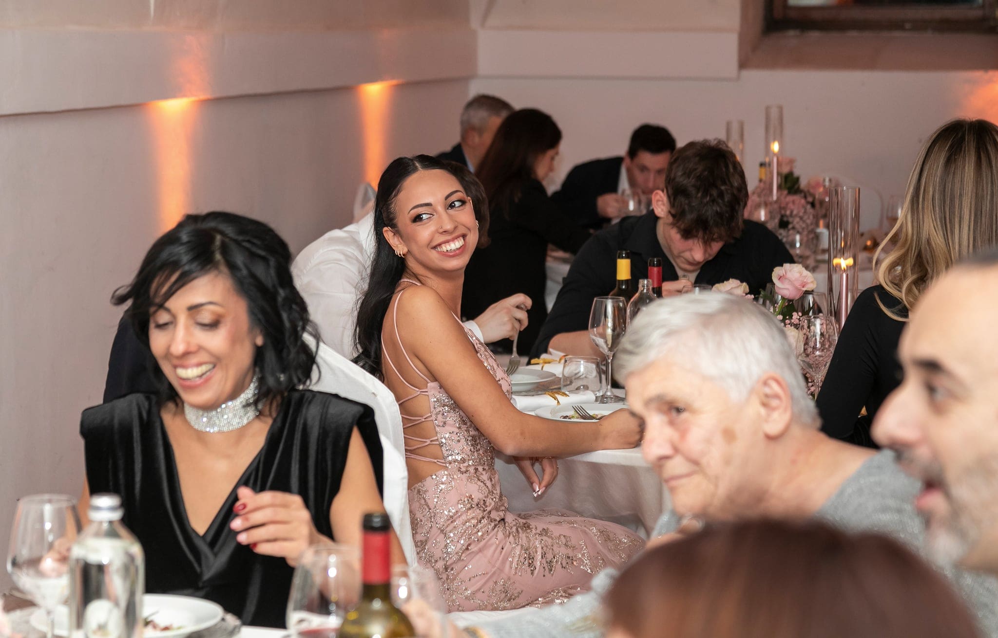 La festeggiata ride al tavolo della cena insieme a una donna dai capelli scuri e ad altri invitati, in un momento spontaneo