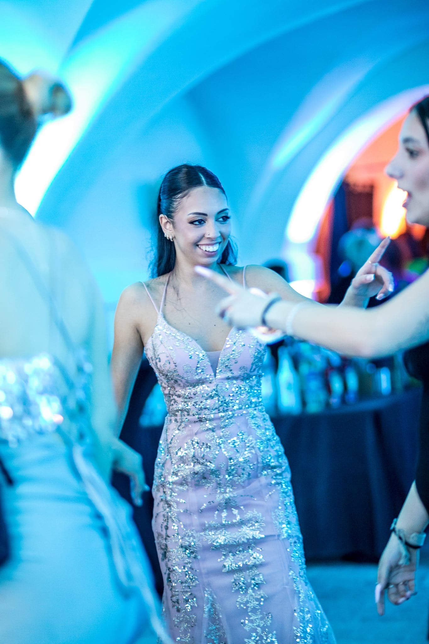 Ragazza in abito rosa brillante sorride mentre balla tra gli invitati, nella sala illuminata da luci azzurre