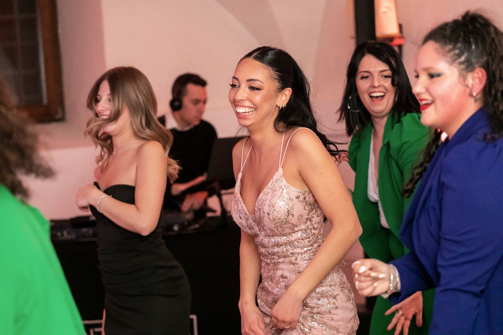 La festeggiata e tre amiche ridono insieme in pista, con il dj in cuffia sullo sfondo e una luce calda sulla sala