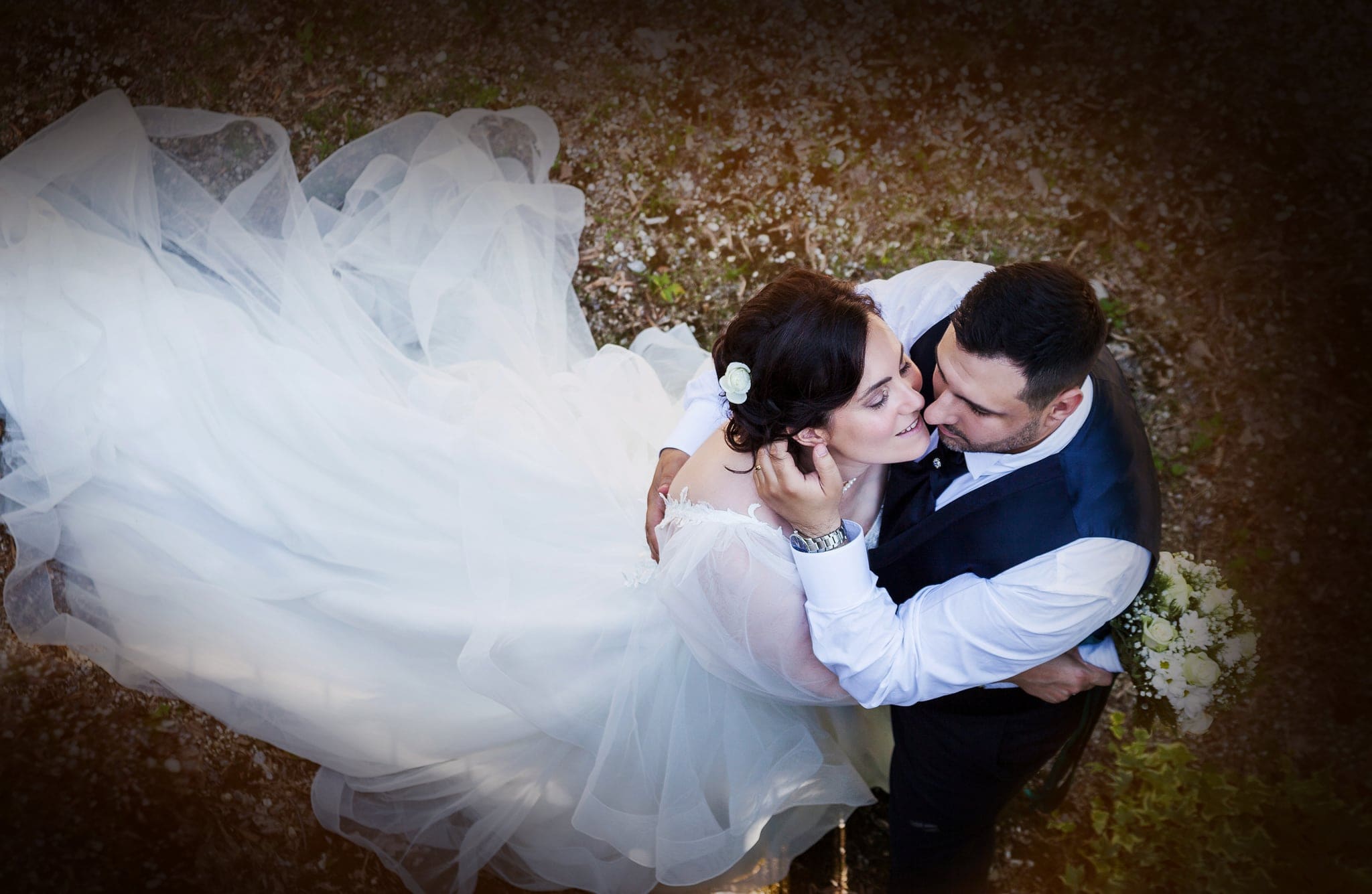 Sposi ripresi dall'alto mentre si baciano sdraiati con il velo di tulle disteso intorno, matrimonio a Pagnacco