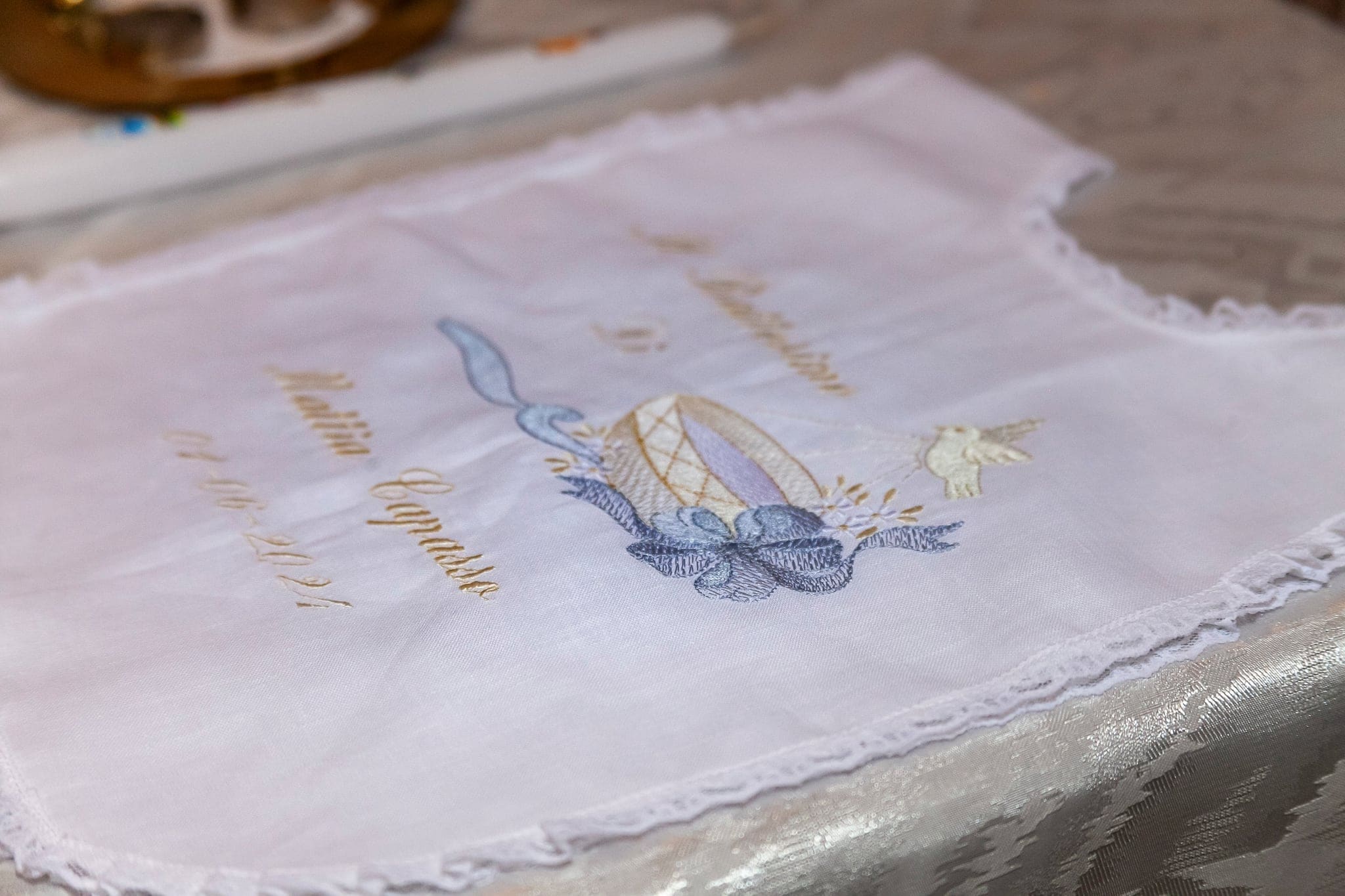 Dettaglio del bavaglino bianco ricamato con pizzo e un ricamo azzurro, preparato per la cerimonia del battesimo