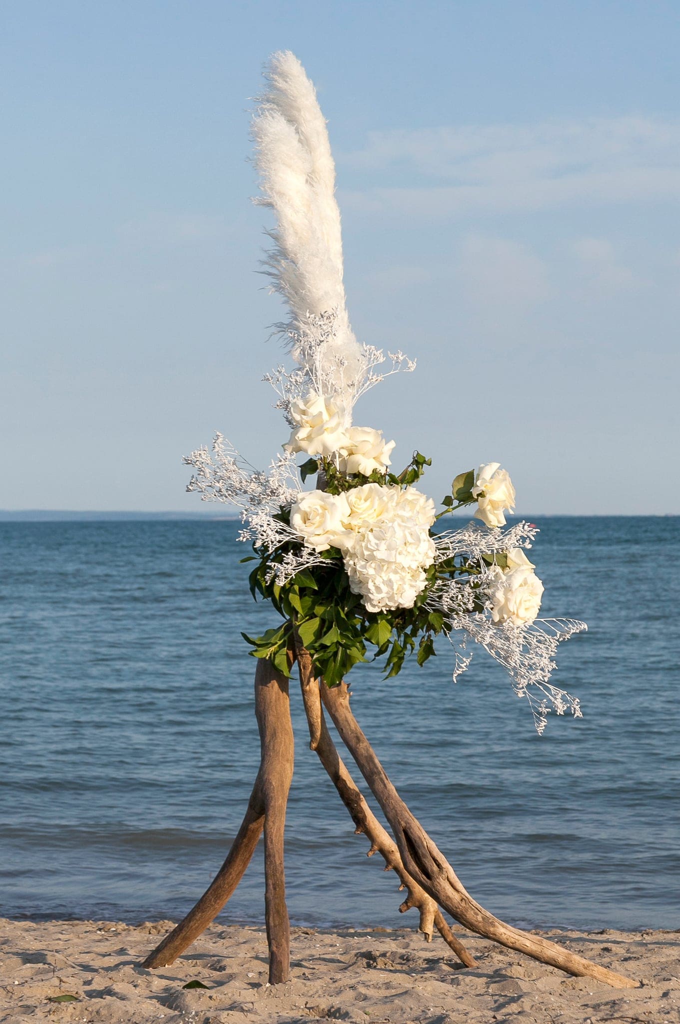 Composizione di fiori bianchi e pampas su sostegno di rami di legno sulla sabbia davanti al mare, matrimonio sulla spiaggia di Grado