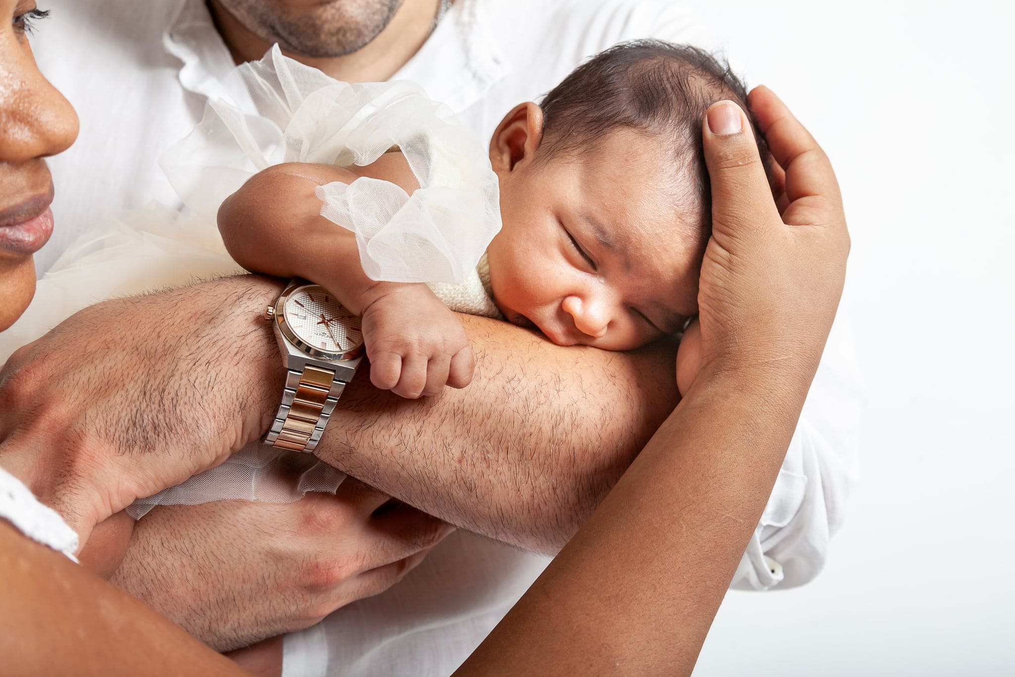 Neonata con abitino di tulle che dorme tra le braccia dei genitori, con la mano della mamma che le sostiene la testa.