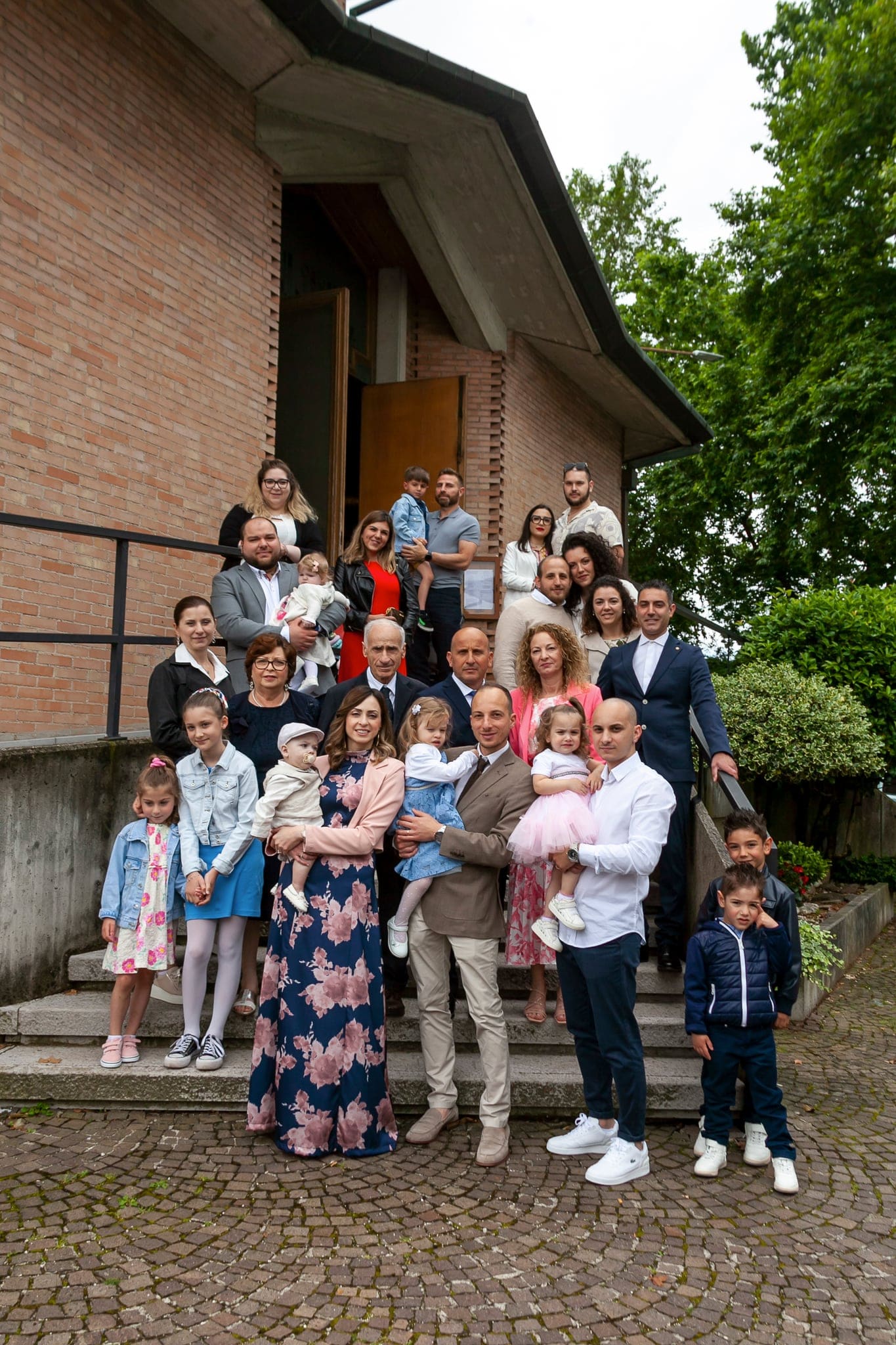 Foto di gruppo con tutta la famiglia, grandi e bambini, sui gradini davanti alla chiesa in mattoni, tra il verde