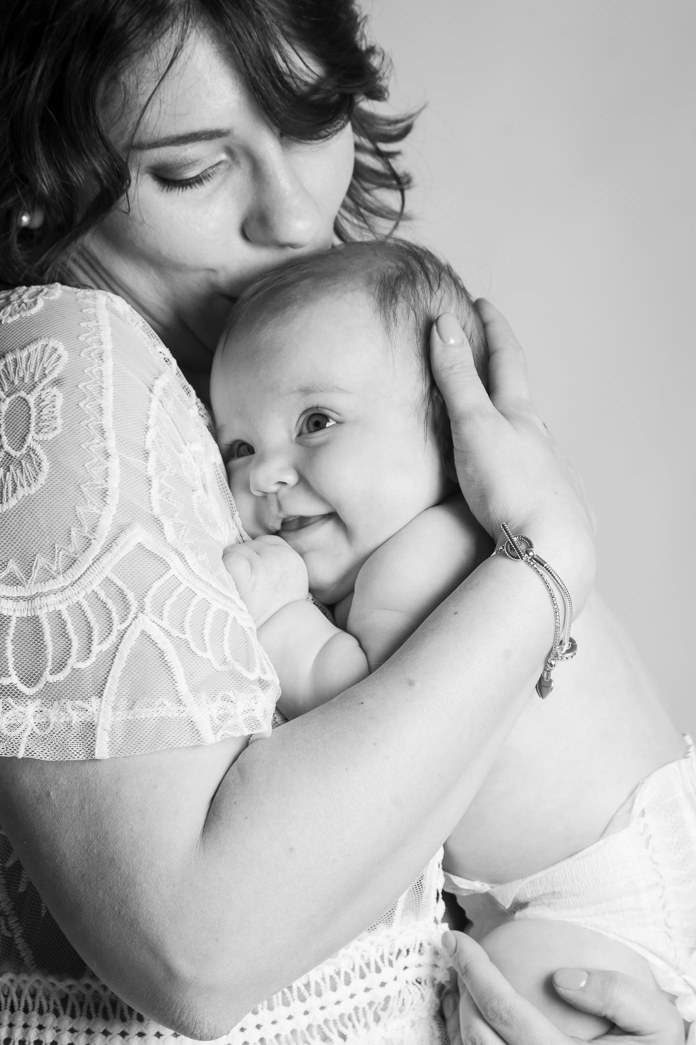 Mamma con camicetta di pizzo che stringe al petto il suo bebè sorridente, in bianco e nero.