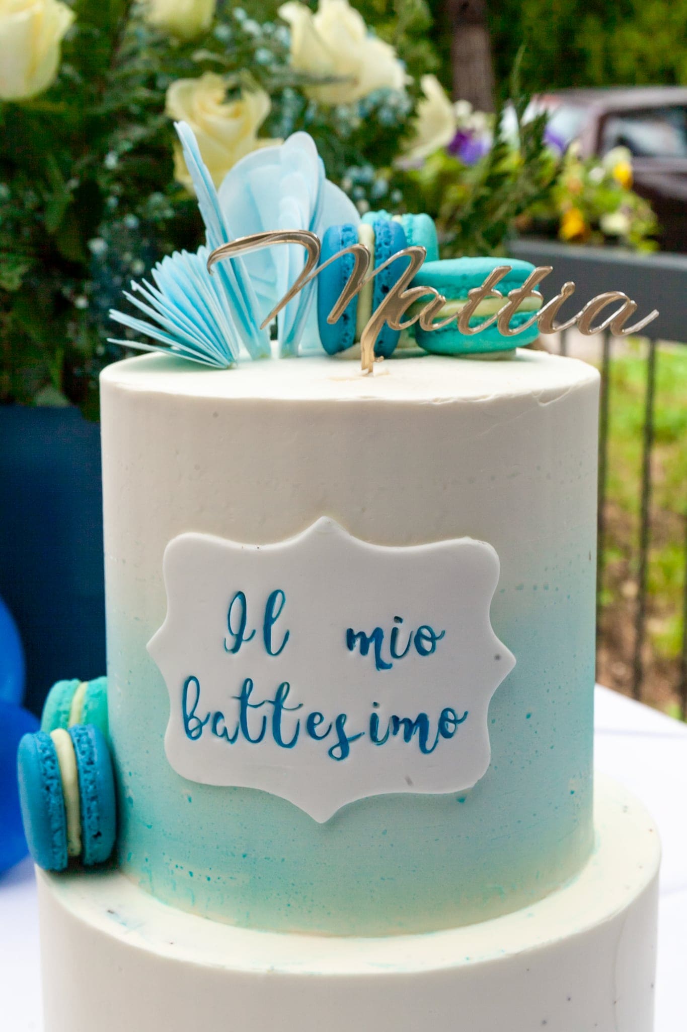Dettaglio della torta bianca e azzurra con la targhetta Il mio battesimo, i macaron e il nome in lettere dorate sopra