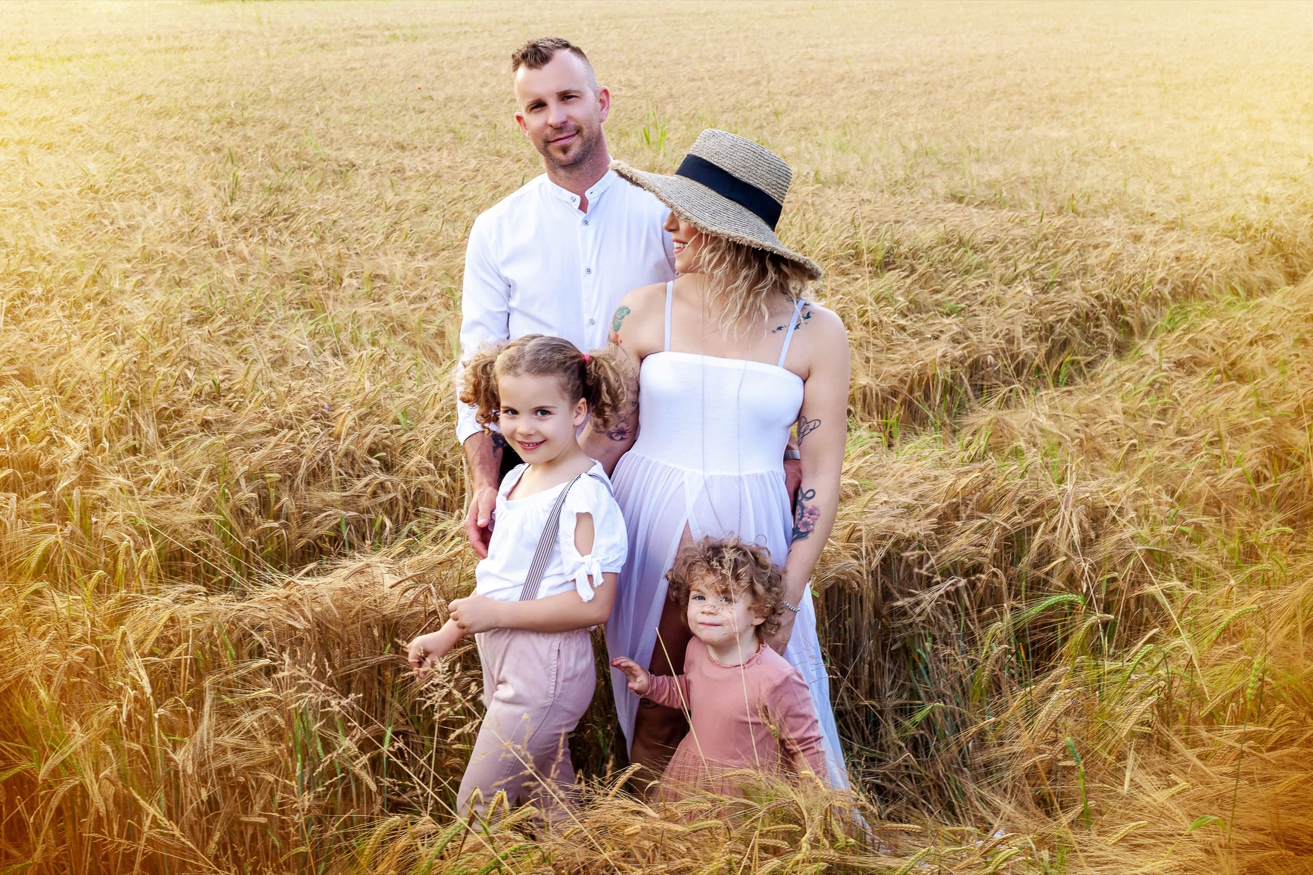Mamma in attesa, papà e due bambine sorridenti in un campo di grano dorato in Friuli